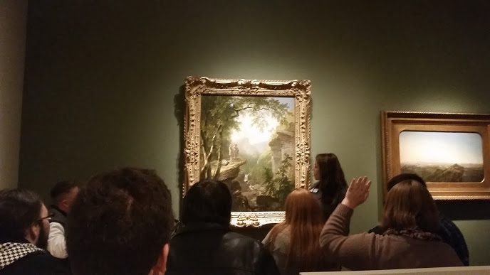 People viewing landscape paintings in a gallery with green walls.