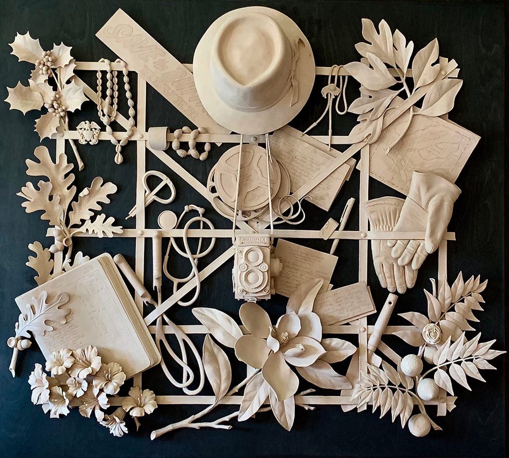 Intricate sculpture collage with hat, camera, gloves, leaves, flowers, notebook on dark background.