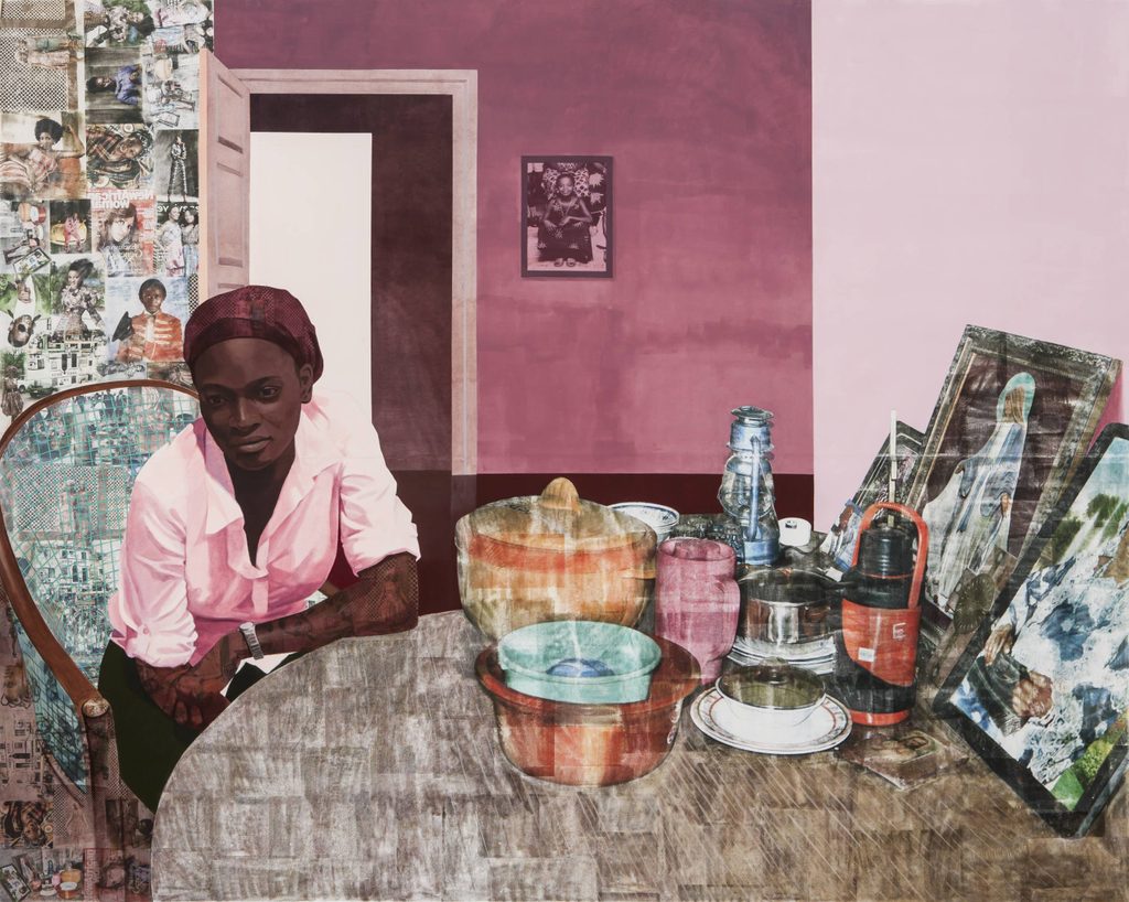Woman in a pink shirt and headscarf sits at table with containers and framed pictures in pink room.