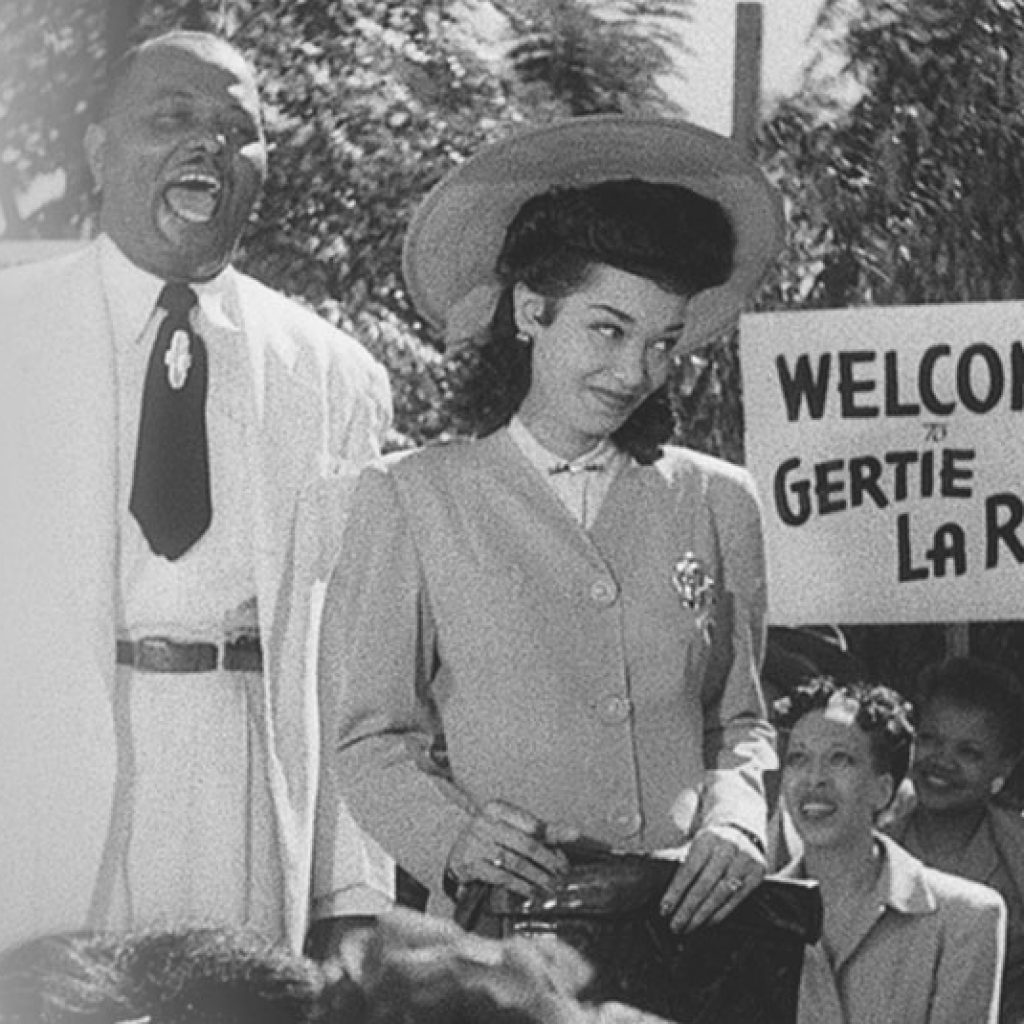 Man and woman at a public event; woman in a hat, man laughing, 