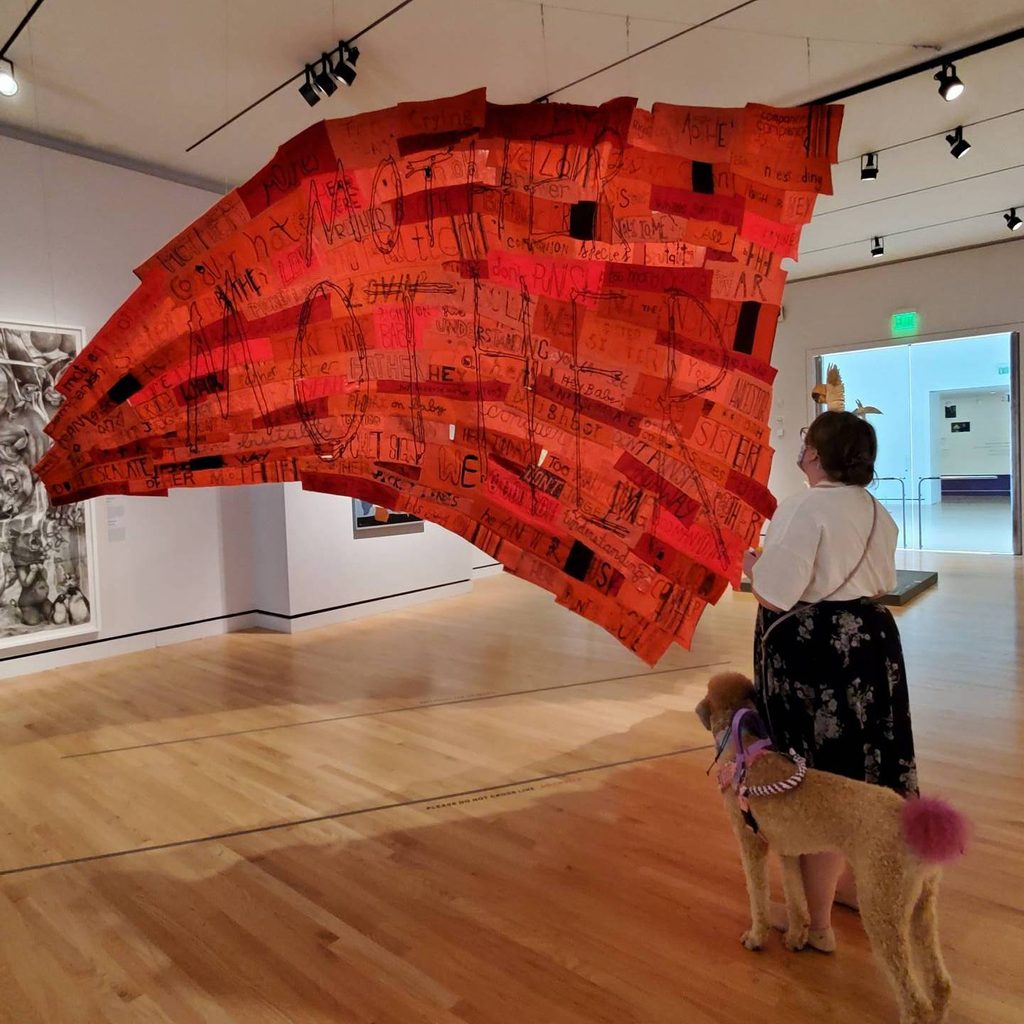 a woman visitor and her support dog look at companion species by marie watt