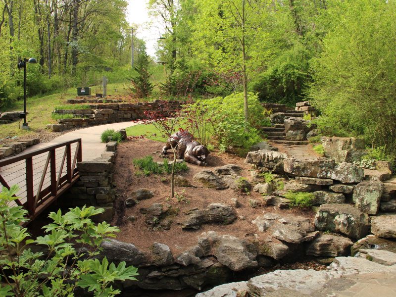 Serene garden with a wooden bridge, rocky landscape, lush greenery, and stone pathways.