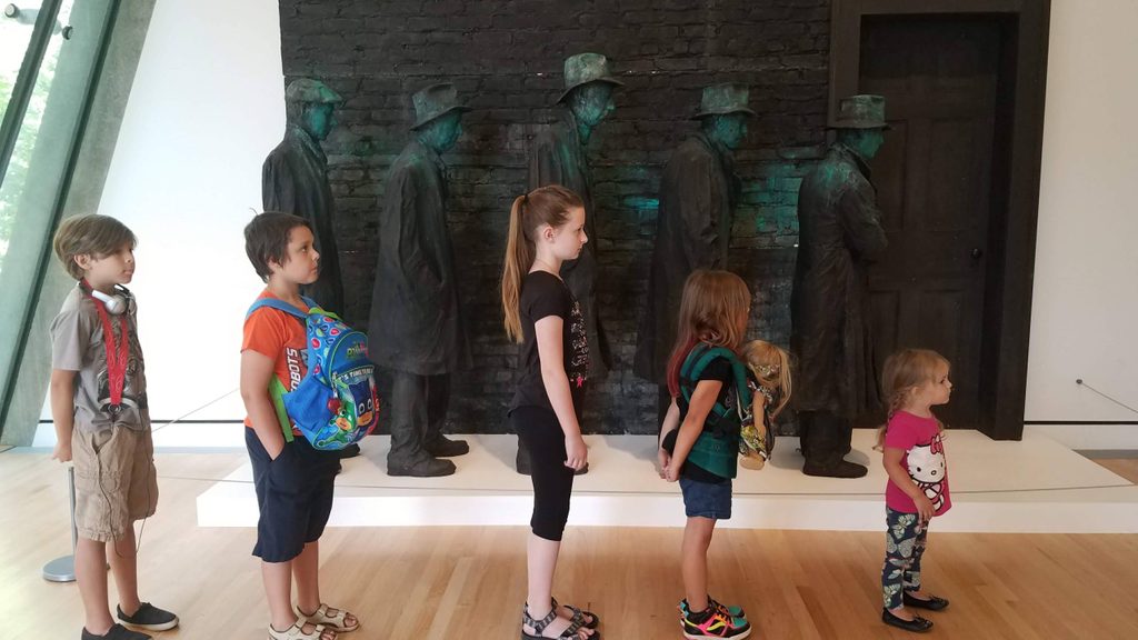 five children visitors pose in front of depression bread line in the galleries
