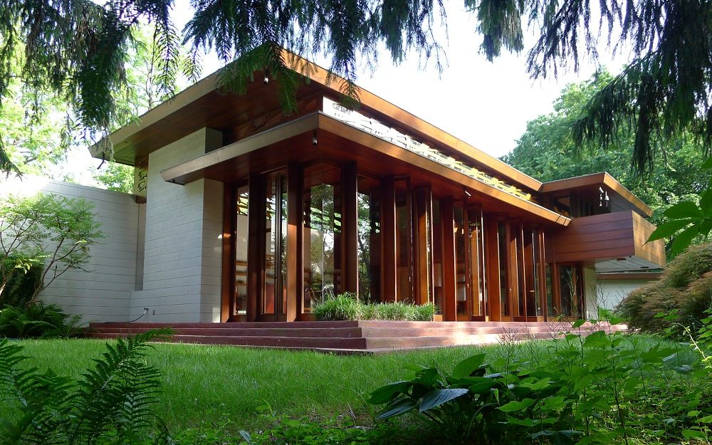 Modern house with flat roof, vertical wood panels, lush greenery, lawn, and entrance steps.