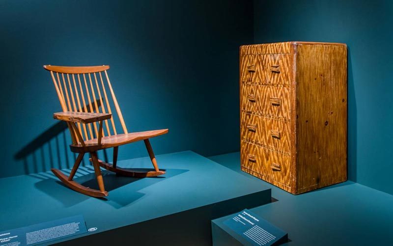 Wooden rocking chair and cabinet in museum with teal walls and informational plaques.