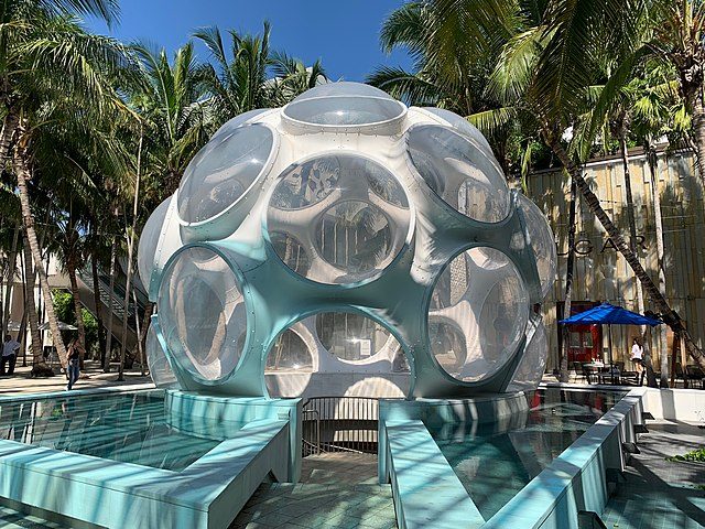 a white dome with circular windows all around it sits outside in a sunny Miami shopping district