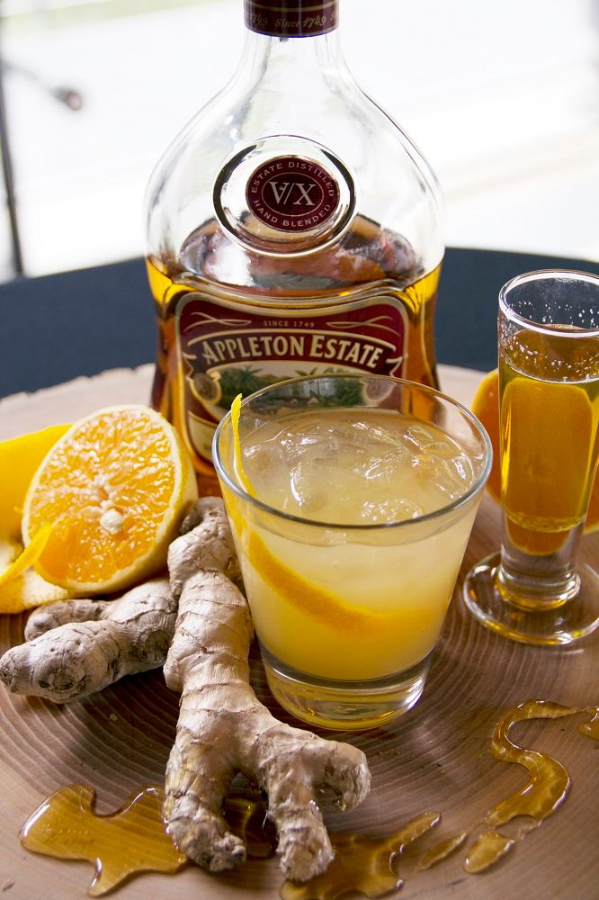 Appleton Estate rum bottle with ginger, sliced orange, and two drinks on a wooden surface.