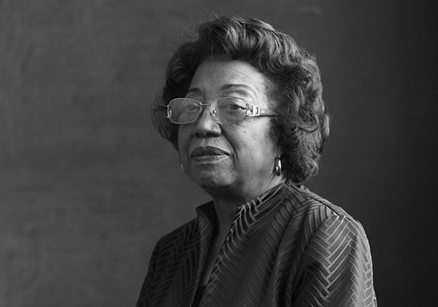 Elderly person with glasses in patterned jacket, monochrome portrait, neutral background.