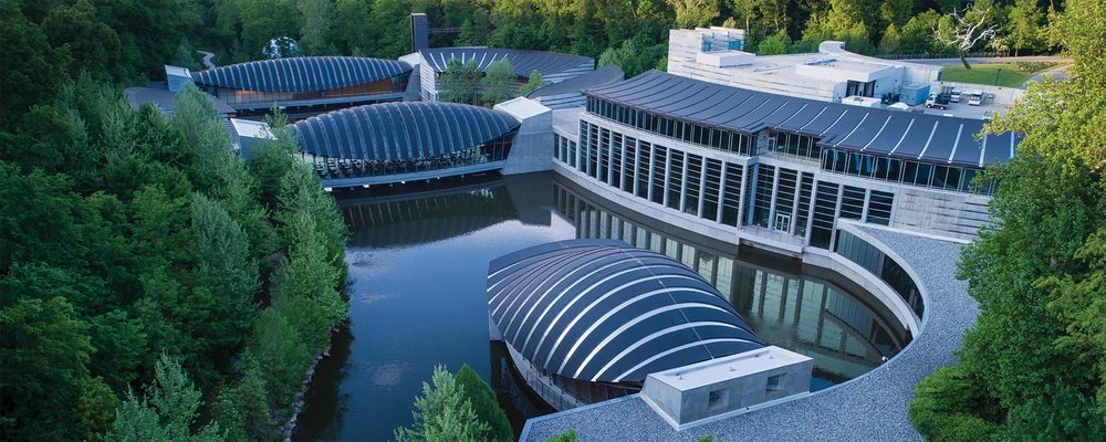 Aerial view of interconnected buildings with curved roofs surrounded by greenery on water.