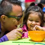 A father and daughter laugh together while working on an art project