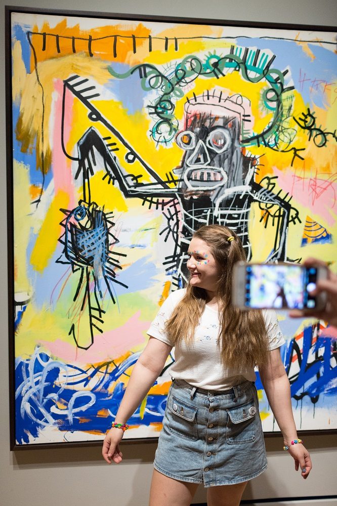Person posing in front of vibrant abstract art with bold lines and colors, photo being taken.