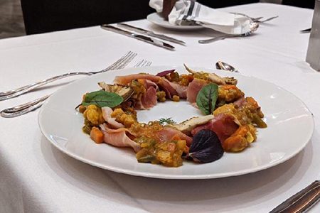 Cured meat slices with colorful vegetables and greens on a white plate, set on a table.