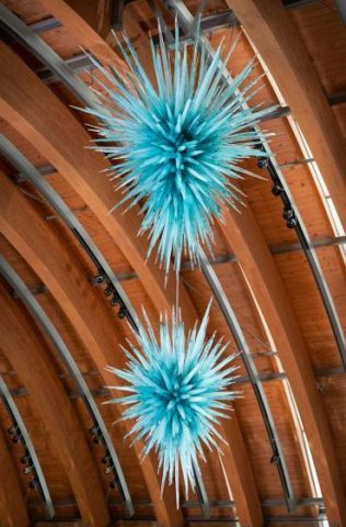 Two spiky blue glass sculptures hang from an arched wooden ceiling.