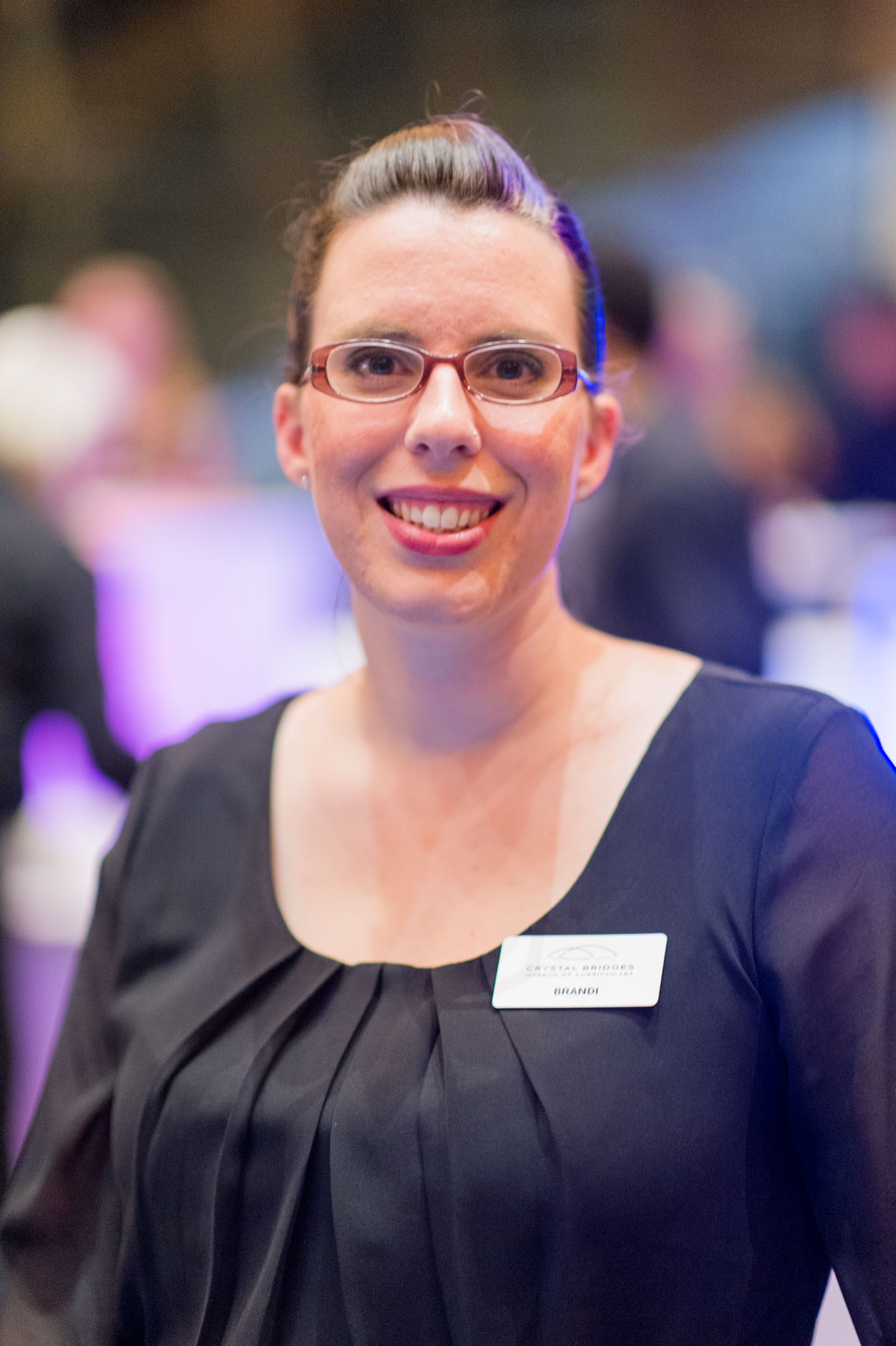 Person in glasses and dark blouse, smiling indoors, wearing 