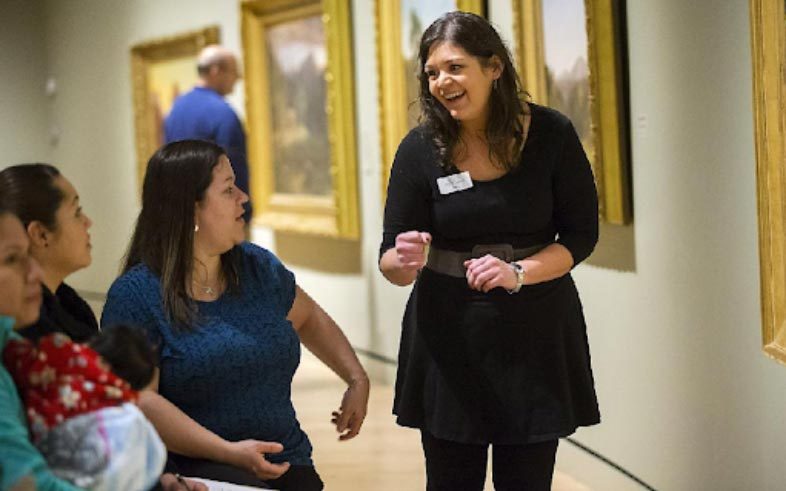 Gallery tour with guide engaging seated visitors near framed artwork.