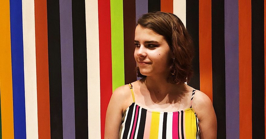 Person in front of colorful vertical striped backdrop, wearing matching striped top.
