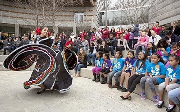 Performer in traditional dress dancing energetically for seated audience in outdoor amphitheater.