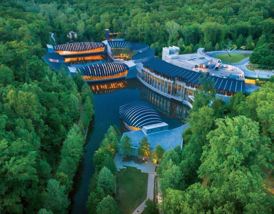 Aerial view of forest-integrated complex with curved roofs, water elements, and lush greenery.
