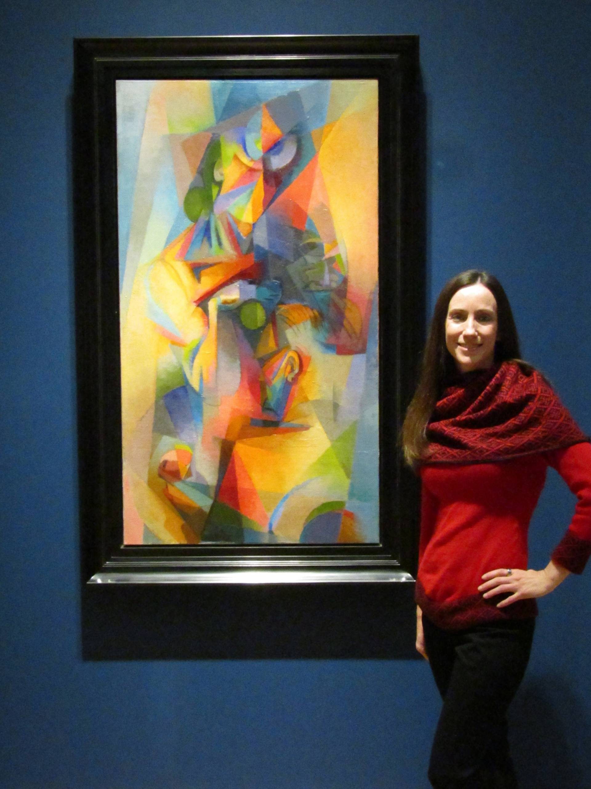 Woman in red next to colorful abstract geometric painting on a blue wall.