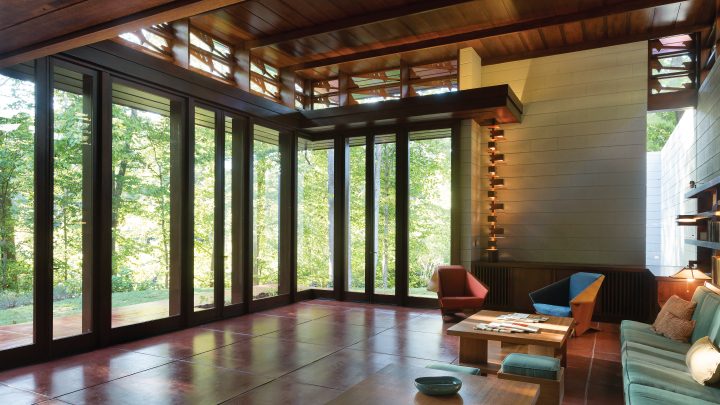 Modern living room with large windows, wooden elements, sofas, and natural light.