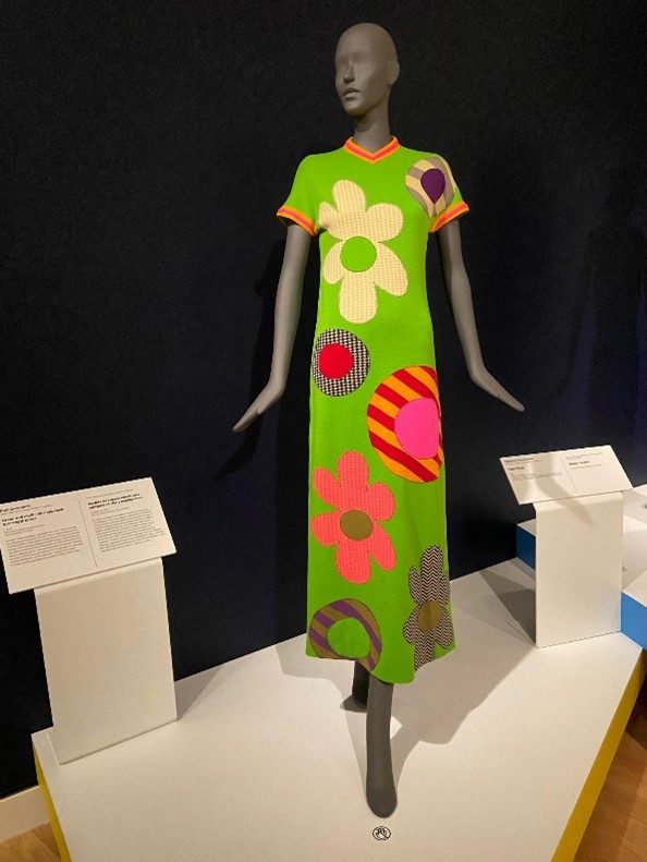 a lime green and multi-color full-length dress with big flowers on a mannequin in a gallery space