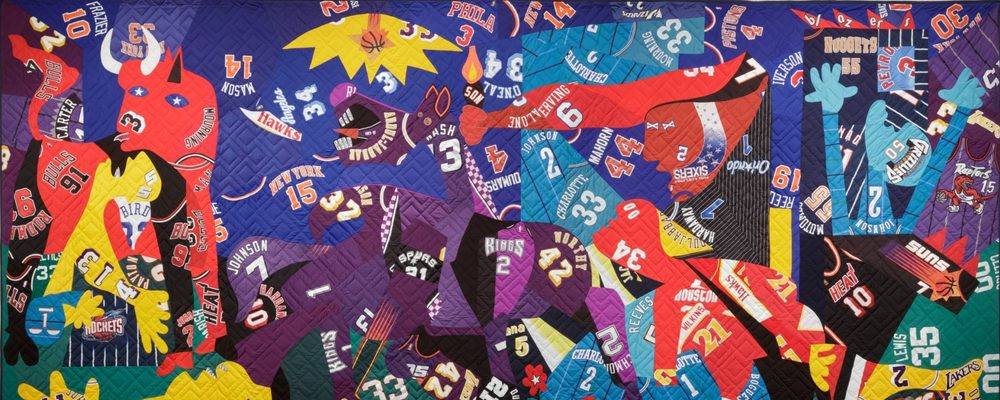 Colorful quilt with abstract basketball jerseys, numbers, logos, and team colors on blue background.