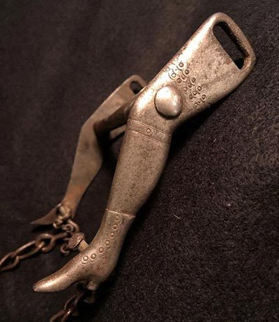 Metal bottle opener shaped like a leg, with intricate designs, attached to a chain.