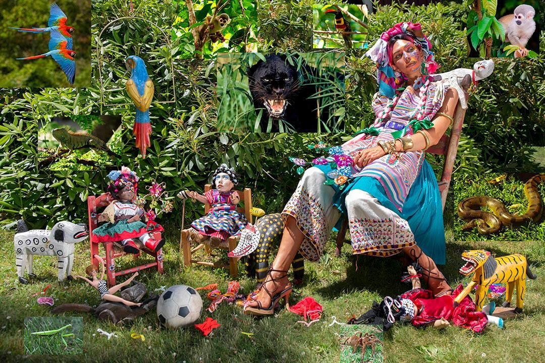 Woman in vibrant attire seated in tropical garden with animals, dolls, and colorful decorations.
