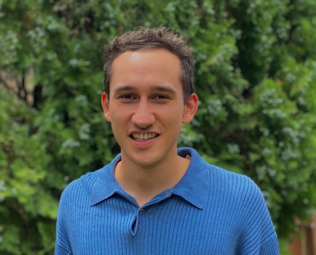 Person in a blue sweater outdoors with green foliage background.