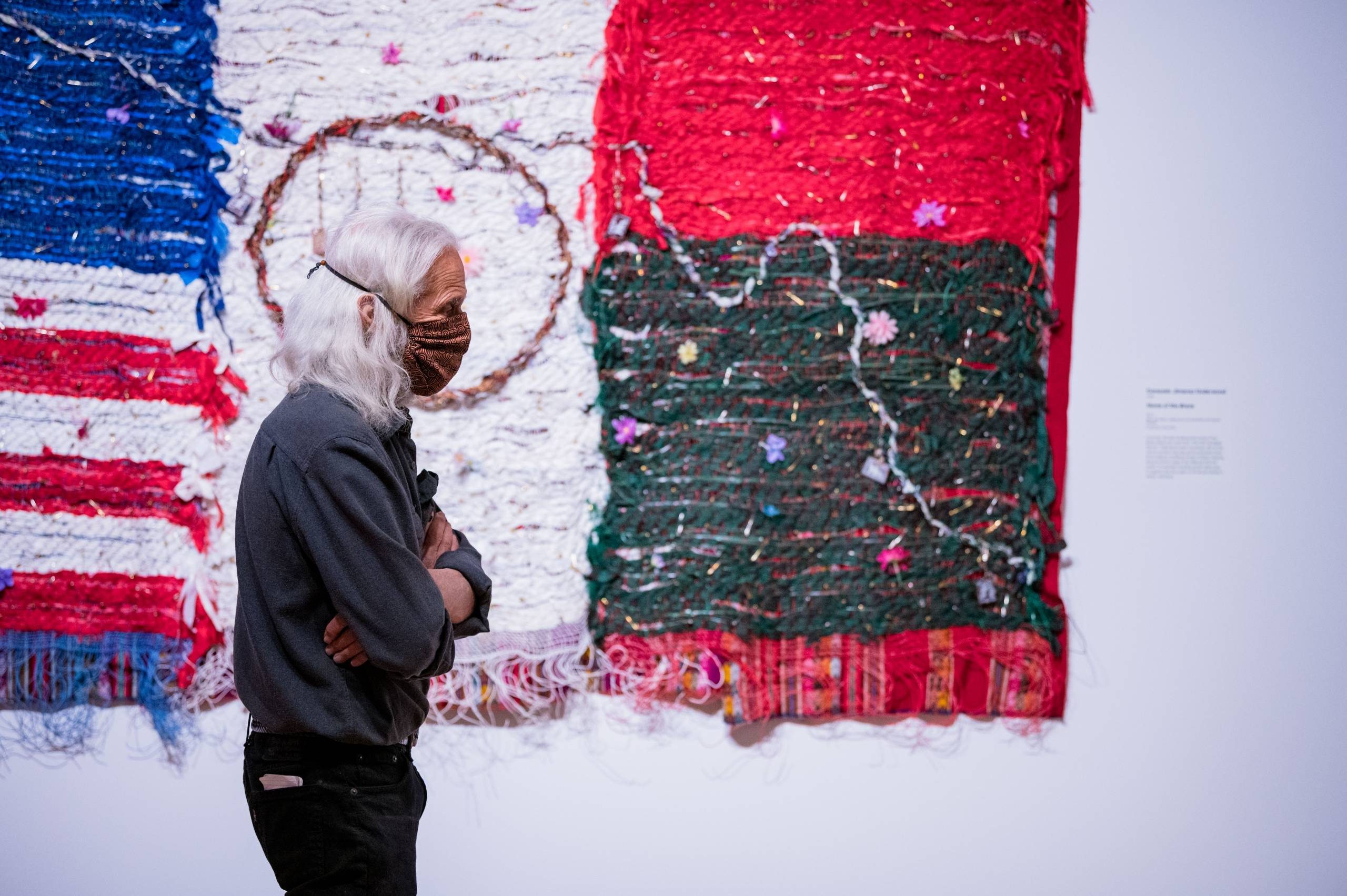 Individual in mask observes colorful textile art with various patterns in a gallery.