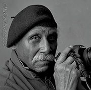 Elderly man in beret holding a camera, black and white portrait.