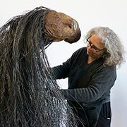 Person crafting large horse-like sculpture with fibrous materials indoors