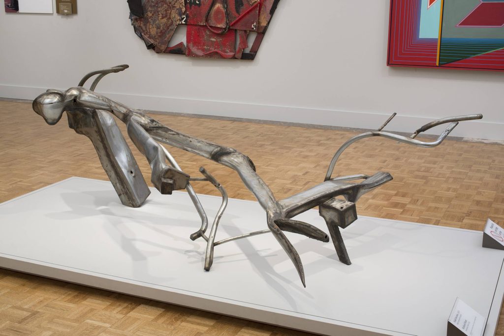 a rusted steel abstract sculpture on a platform in an art gallery