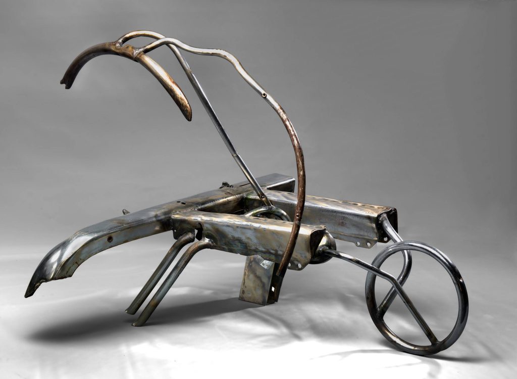 a rusted steel sculpture in the shape of a wheelbarrow and a car bumper