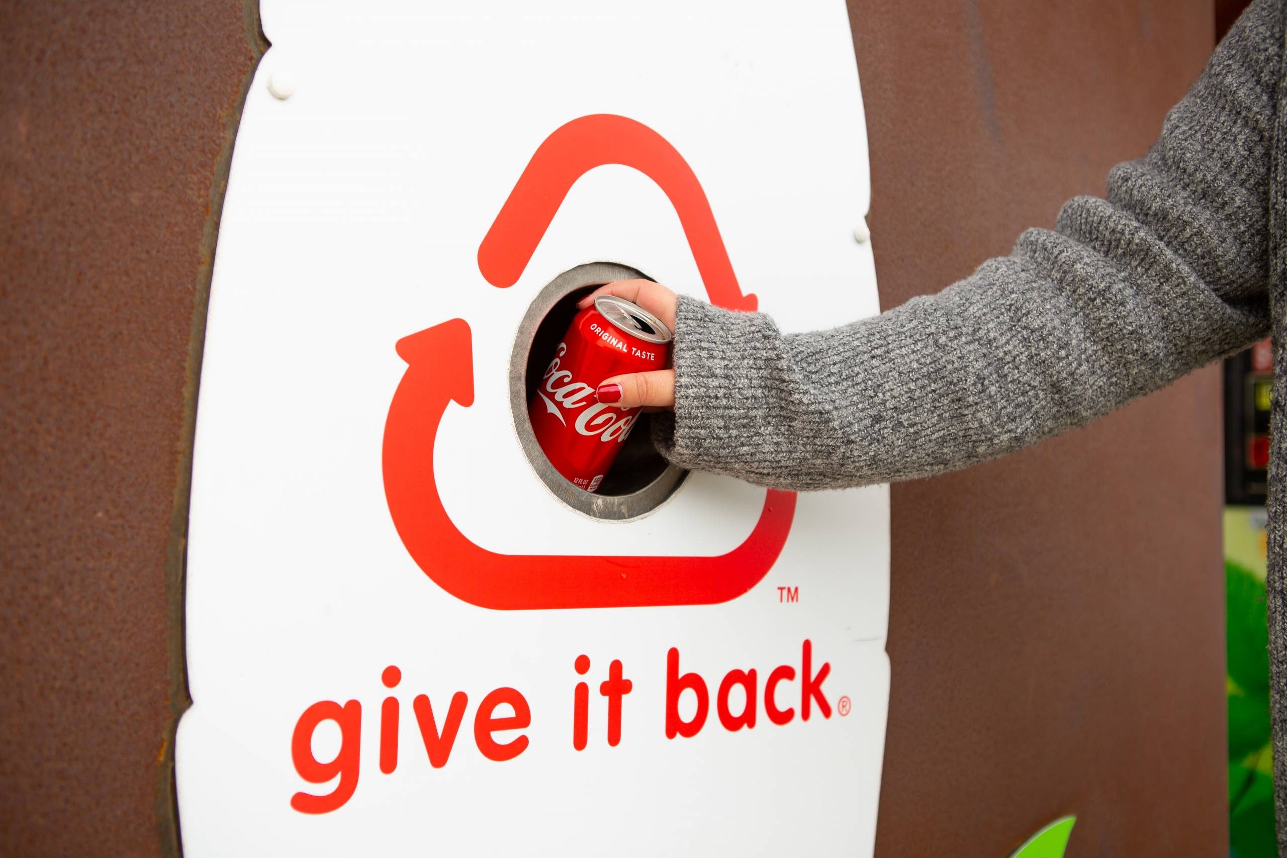 A person recycling a Coca-Cola can in a bin labeled 
