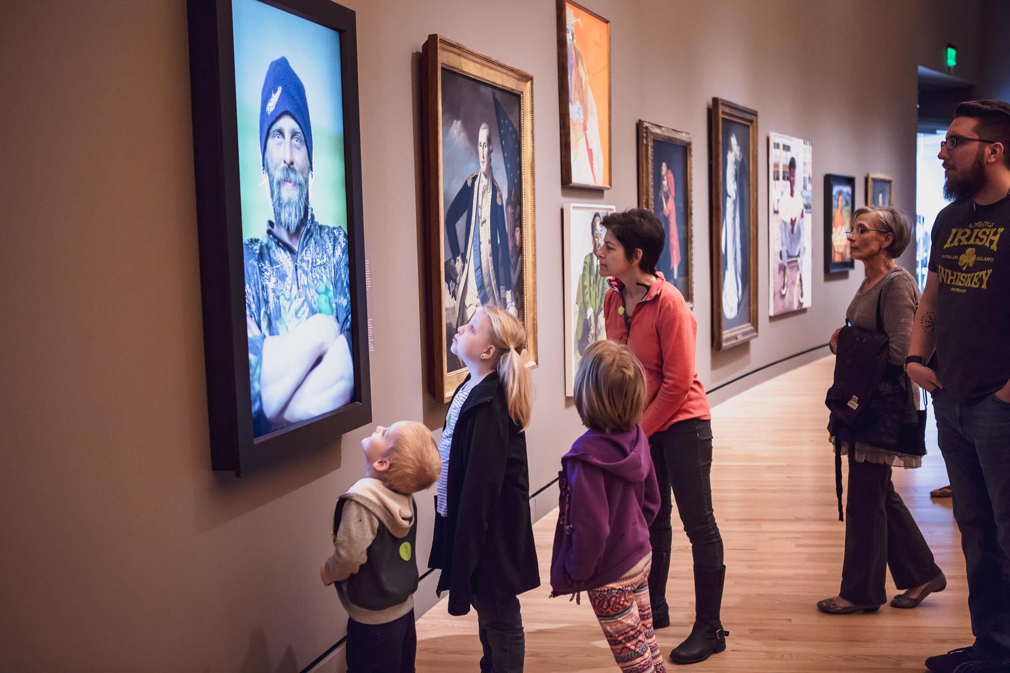 Group in gallery viewing digital and traditional art displays on modern wooden flooring.