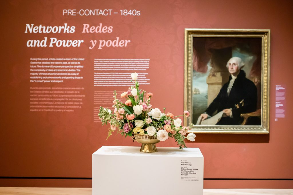 Low vase of pastel flowers on a pedestal in front of a portrait of George Washington