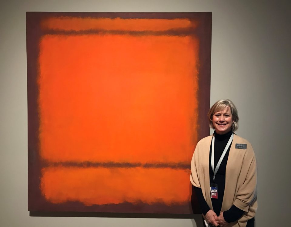 Person beside an abstract painting with orange and brown rectangles, wearing a lanyard and badge.