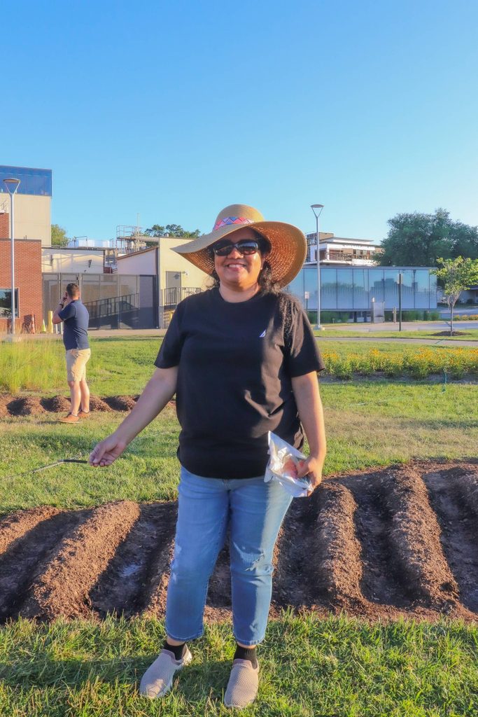 a woman in a sunhat poses in front of planted marigolds at the momentary