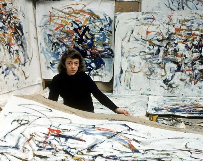 Individual in a studio surrounded by large, vibrant abstract paintings with dynamic brushstrokes.