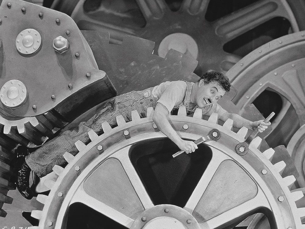 Person in overalls with wrenches among large gears, in an industrial setting, playful expression.