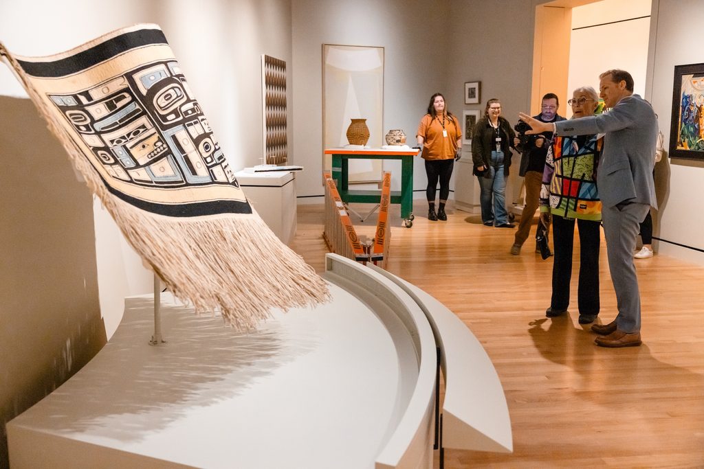 People observing art displays in a gallery with textile pieces and sculptures on wooden floors.