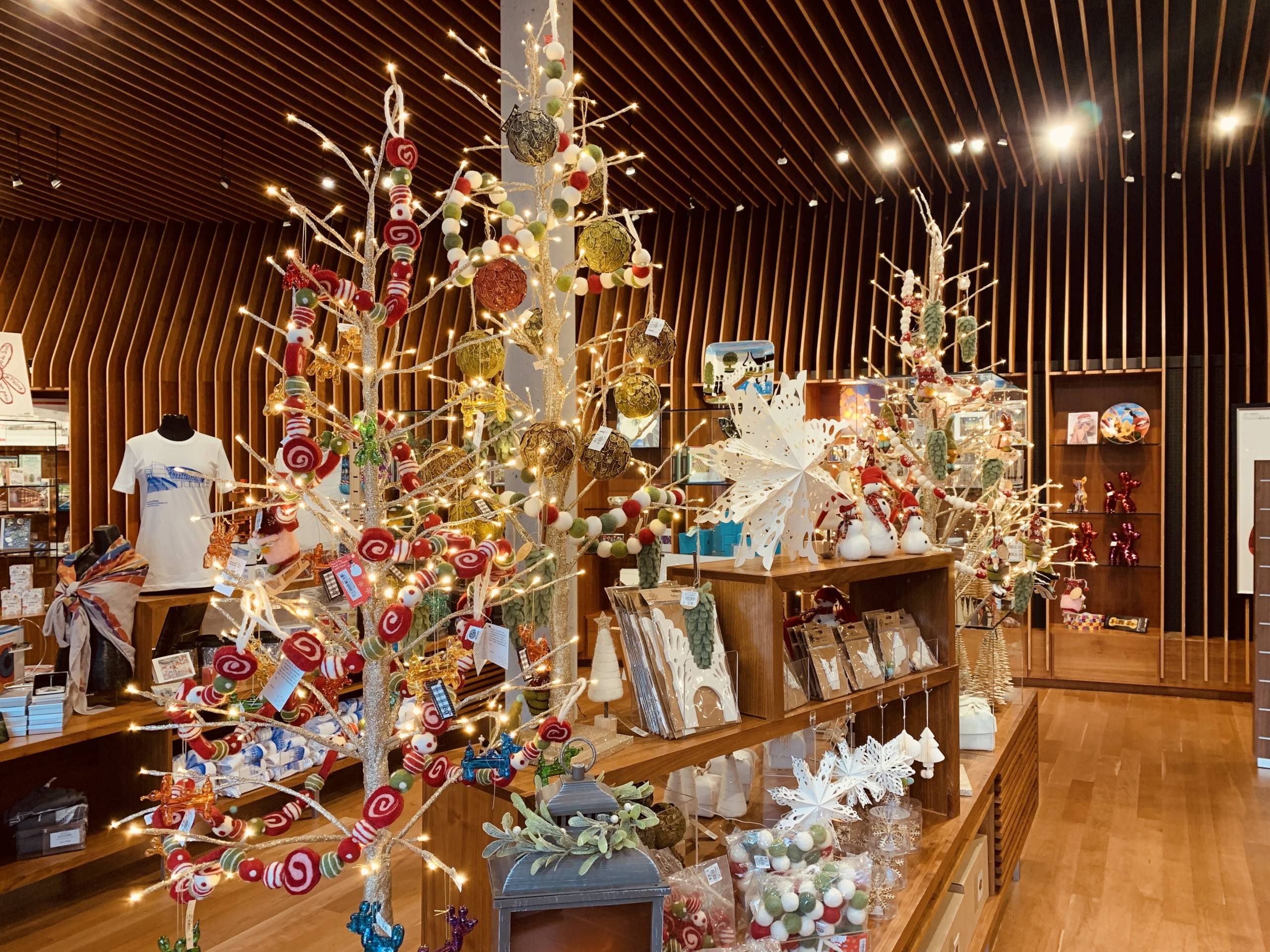 an image of the museum store's holiday decor, including trees decorated with colorful garland and paper snowflakes