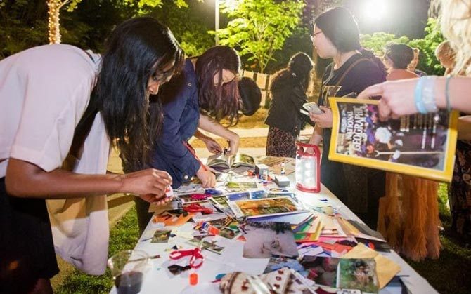 People crafting at an illuminated outdoor table with magazines and materials, trees in background.
