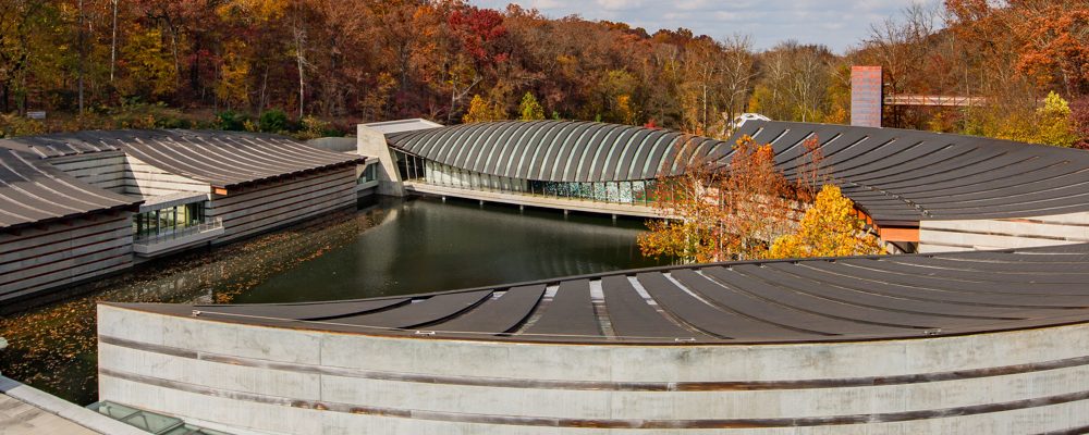 Modern complex with curved roofs, central water body, and surrounding autumn forest.
