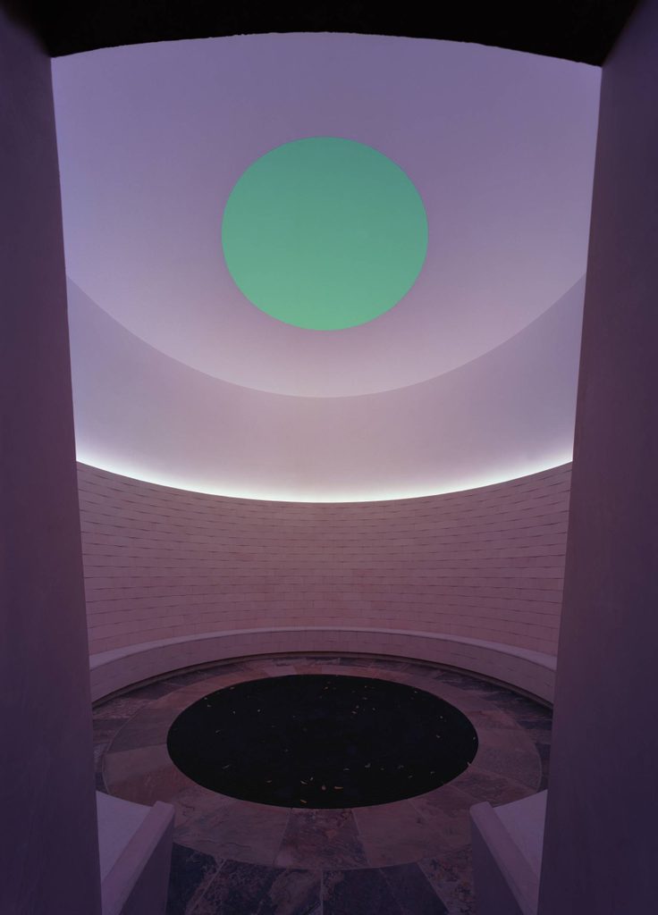 Circular room with light brick walls, stone tile floor, central black circle, and green ceiling light.