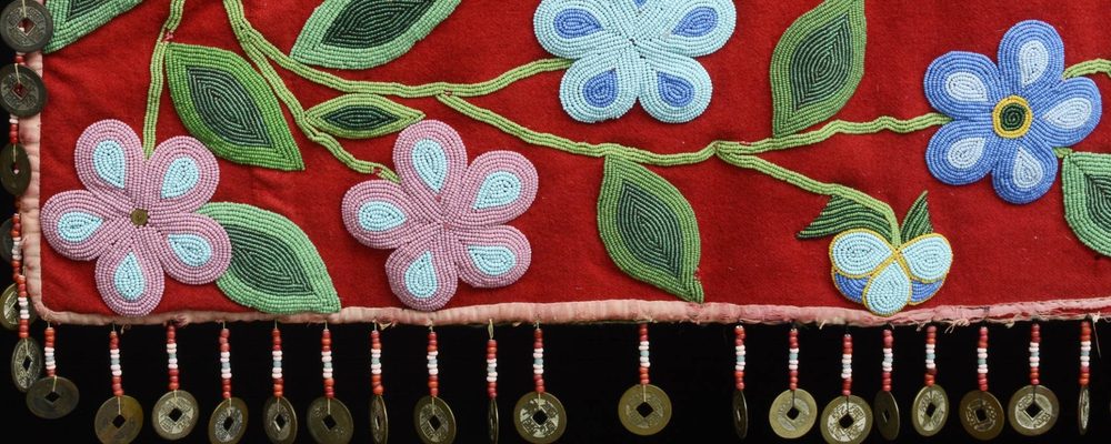 Decorative textile with colorful beadwork flowers, leaves on red fabric, and metal token fringe.