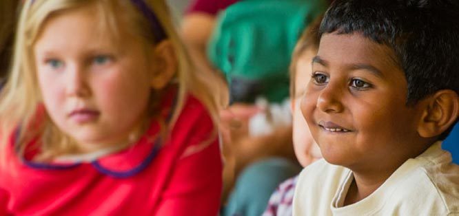 Two children sitting, facing forward, one smiling, engaging with something off-frame.