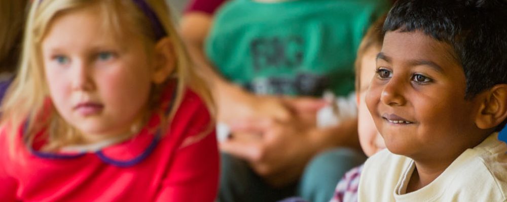 Children seated indoors, attentively looking forward, focused on expressions and engagement.