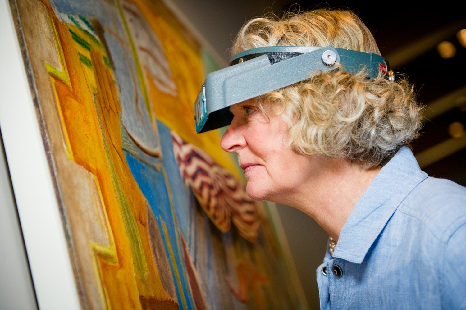 Person inspecting colorful abstract painting with magnifying visor.